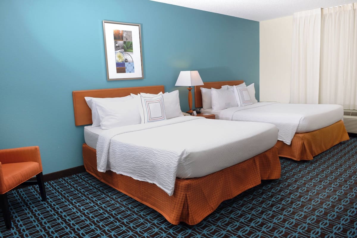 A hotel room with two beds, a single chair, a framed picture on the wall, and a patterned carpet.