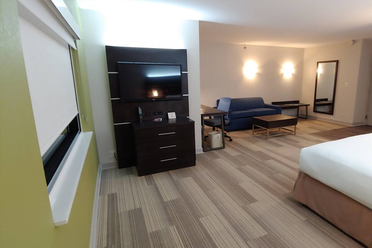 A hotel room with a bed, a desk, a chair, a sofa, a TV, and a wardrobe.