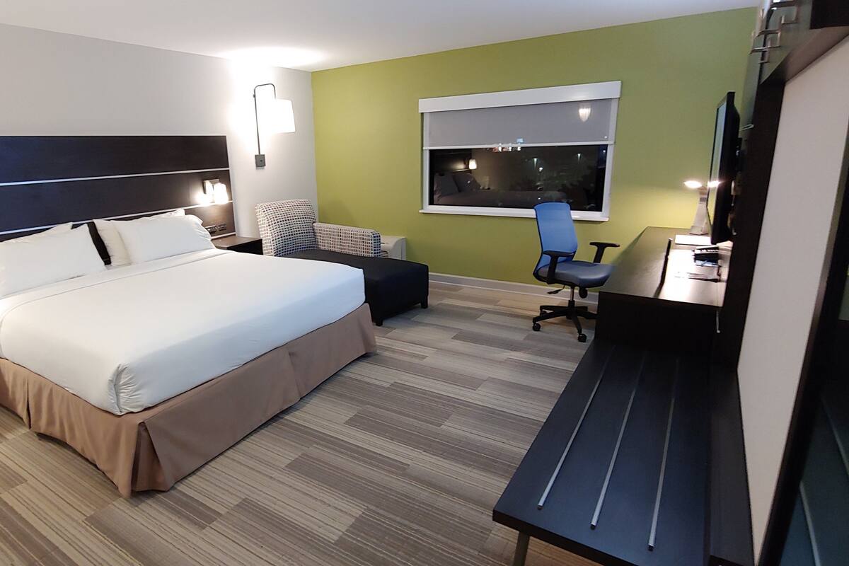 A hotel room with a bed, a desk, a chair, a window, and a TV.