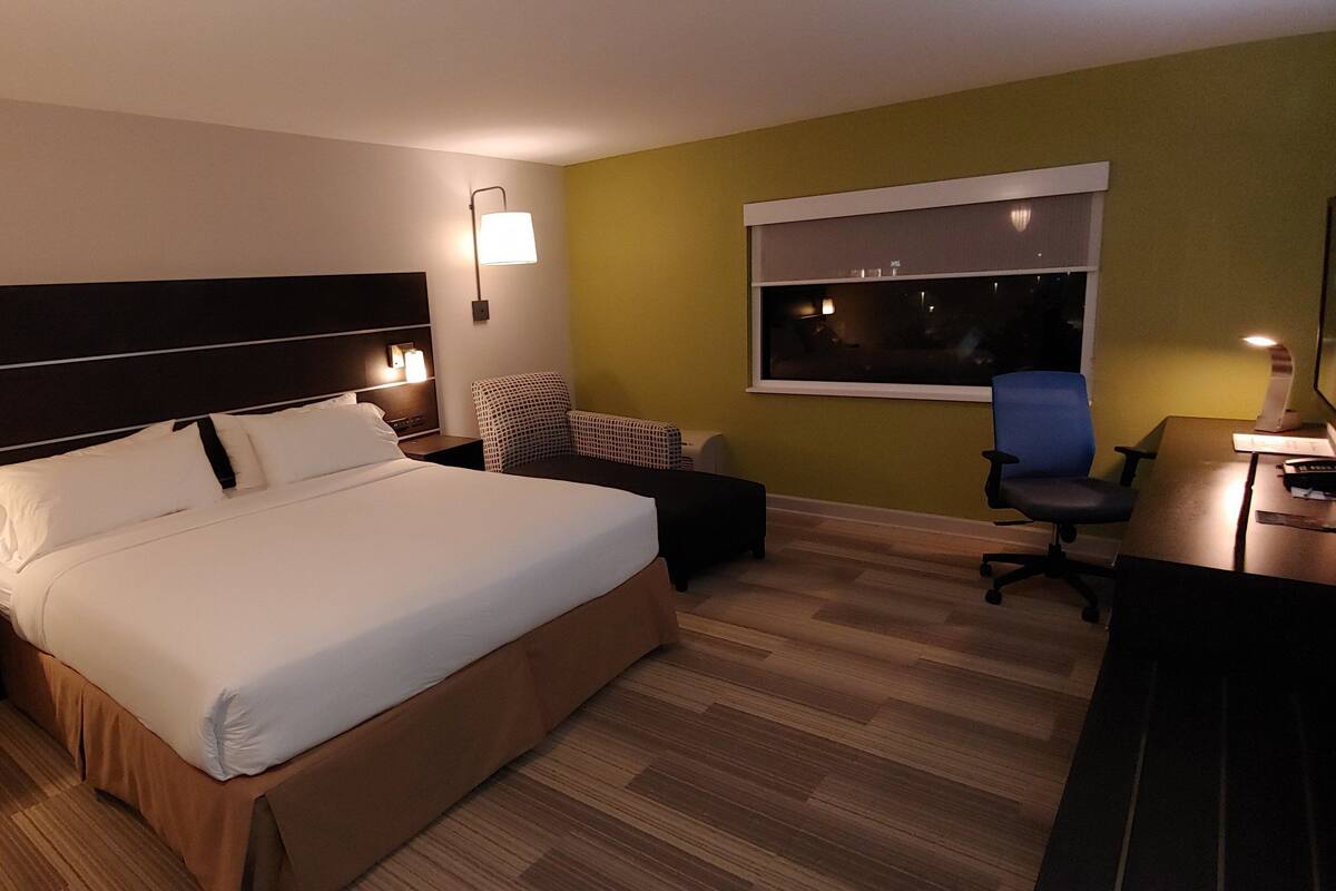 A hotel room with a large bed, a desk, a chair, and a window.
