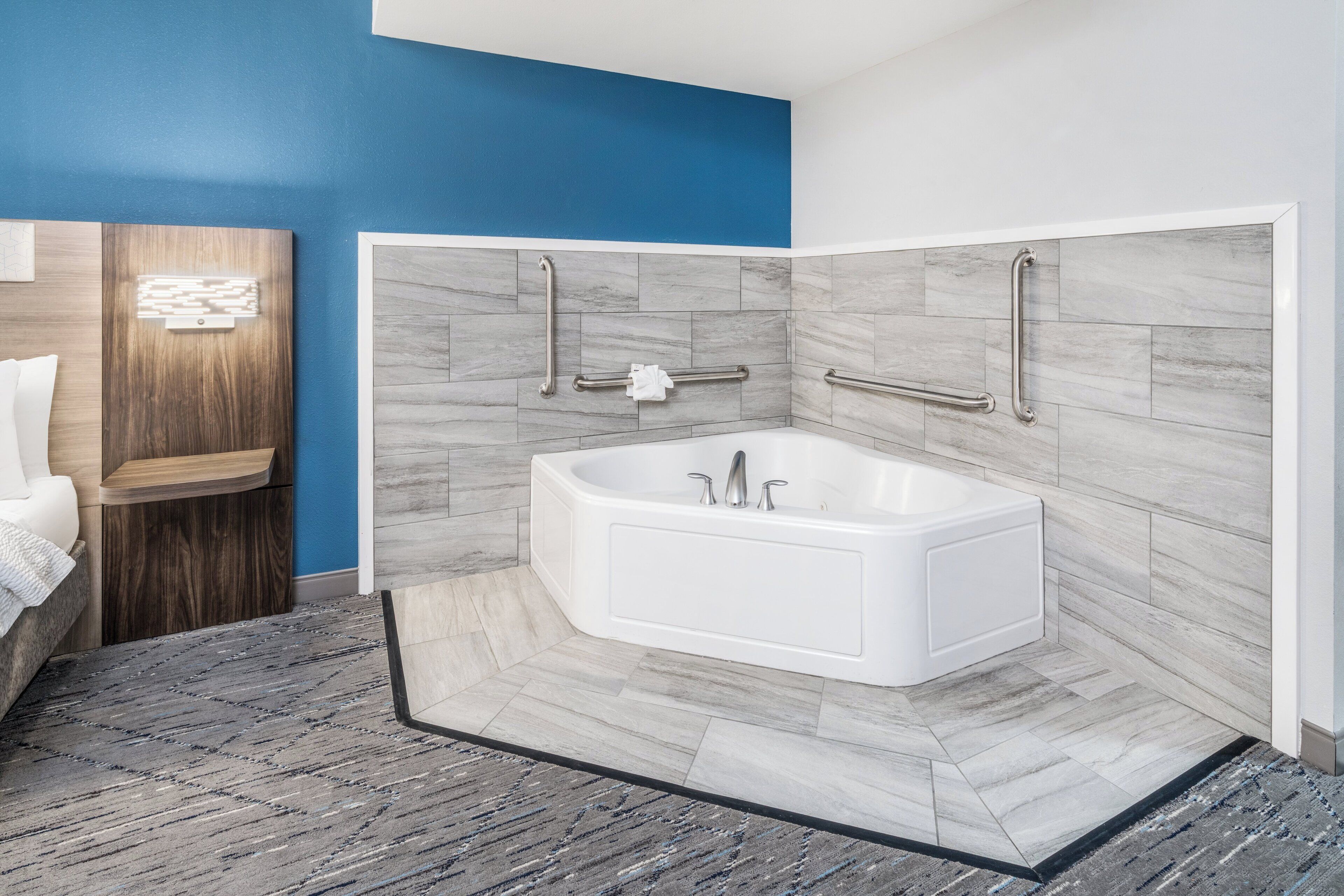 Un baño moderno con una bañera independiente, barras de apoyo y un tocador de madera.