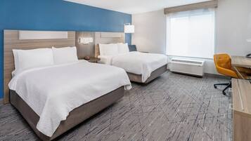A hotel room with two beds, a desk, an air conditioner, and a window.