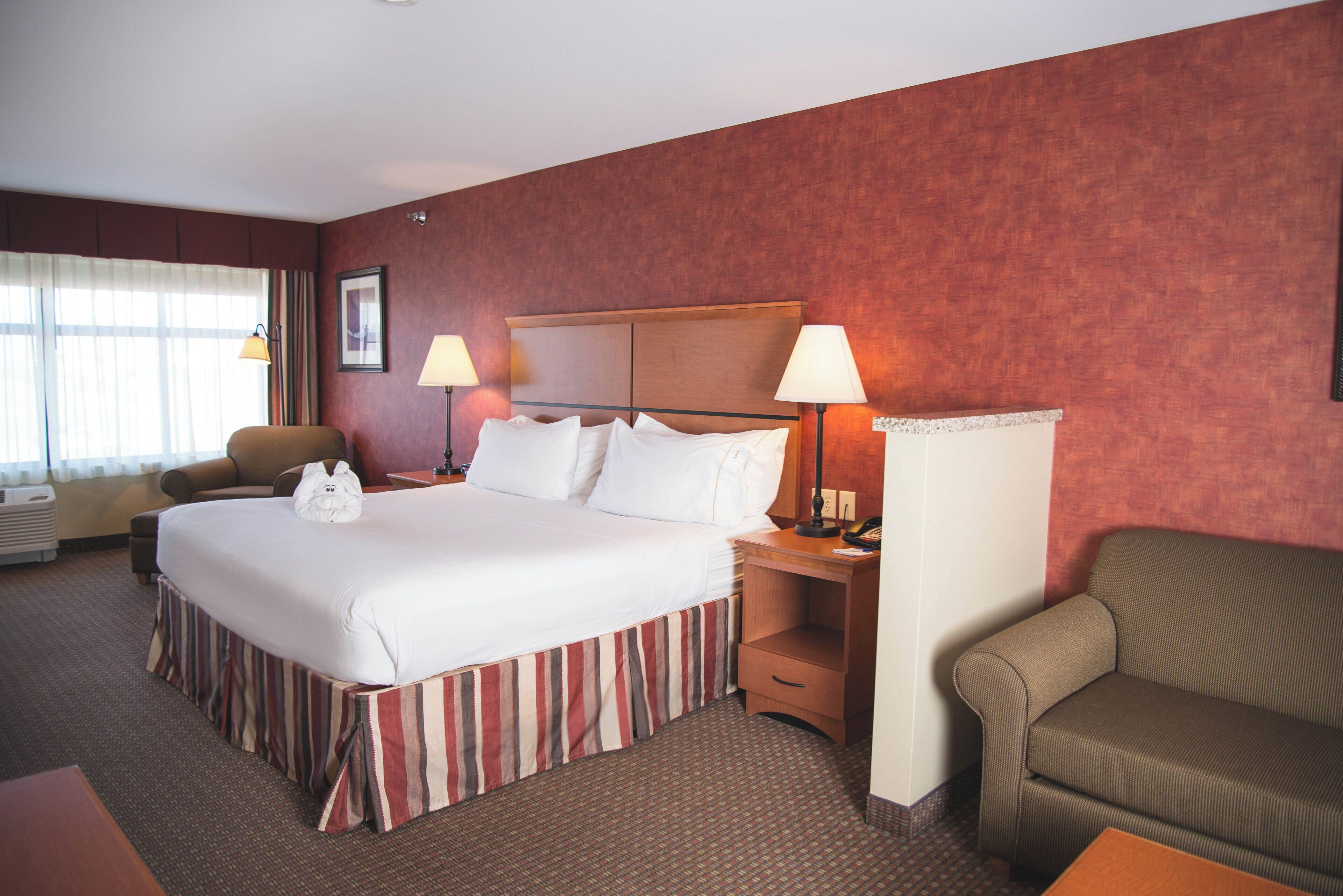 A hotel room with a large bed, two bedside lamps, a chair, a sofa, and a desk with a telephone.