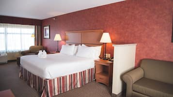 A hotel room with a large bed, two bedside lamps, a chair, a sofa, and a desk with a telephone.