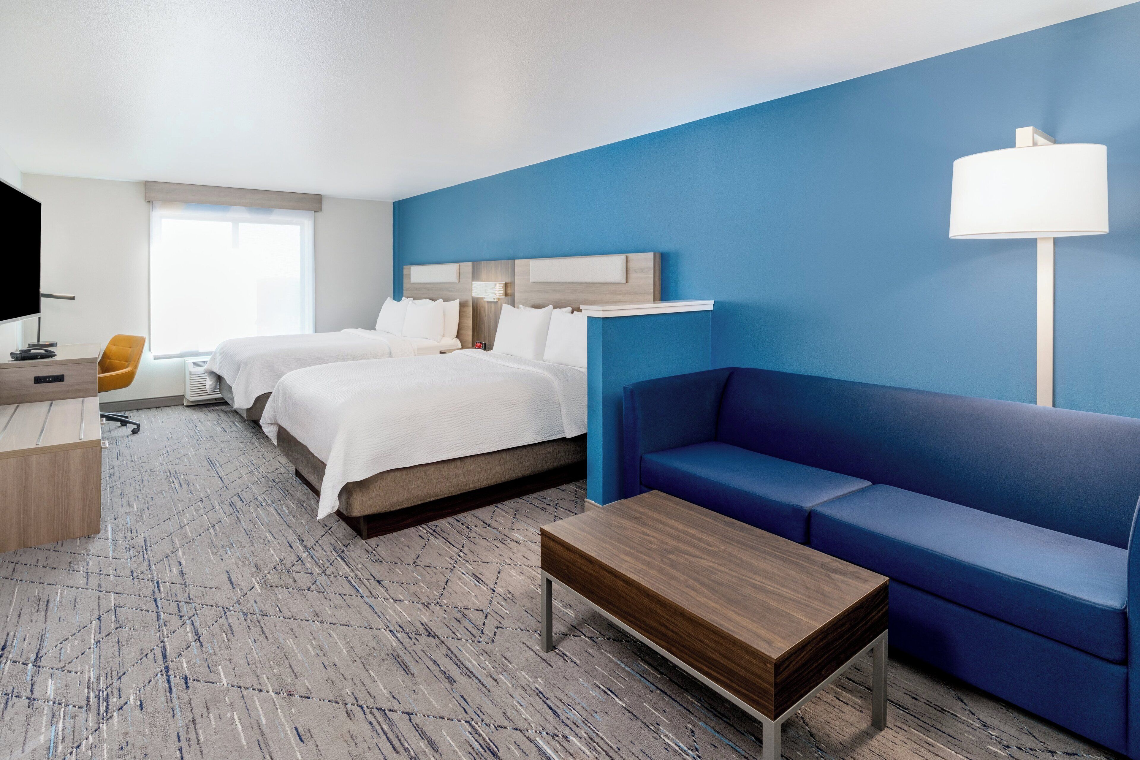 Habitació d'hotel amb dos llits, un sofà blau, una taula de centre de fusta, un escriptori amb una cadira i una televisió.