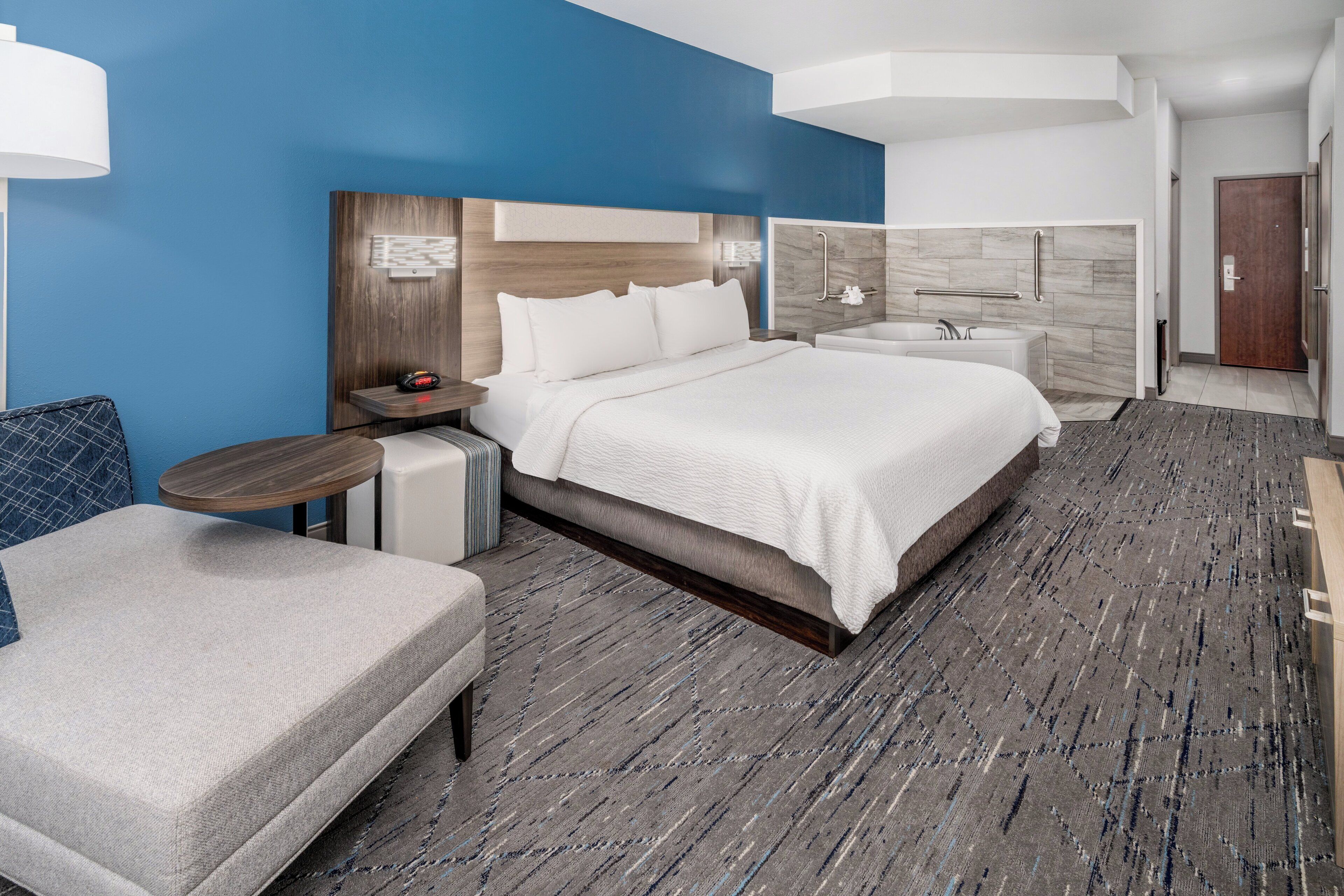 A modern hotel room with a large bed, bedside tables, a seating area, a bathroom with a bathtub, and a shower.
