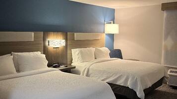 A hotel room with two beds, a nightstand, a lamp, and a ceiling light.