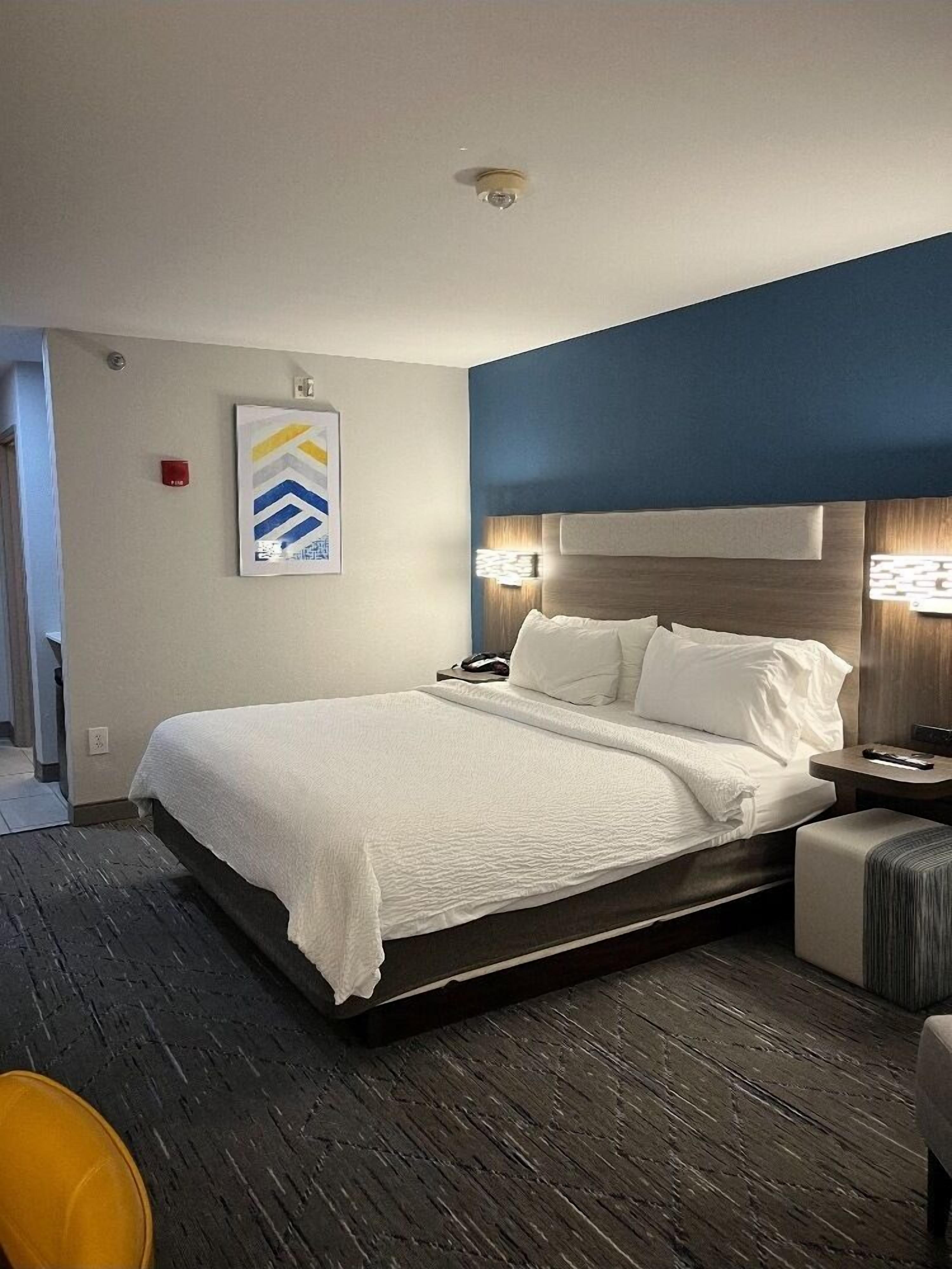 A hotel room with a large bed, a bedside table, a chair, and a wall-mounted artwork.