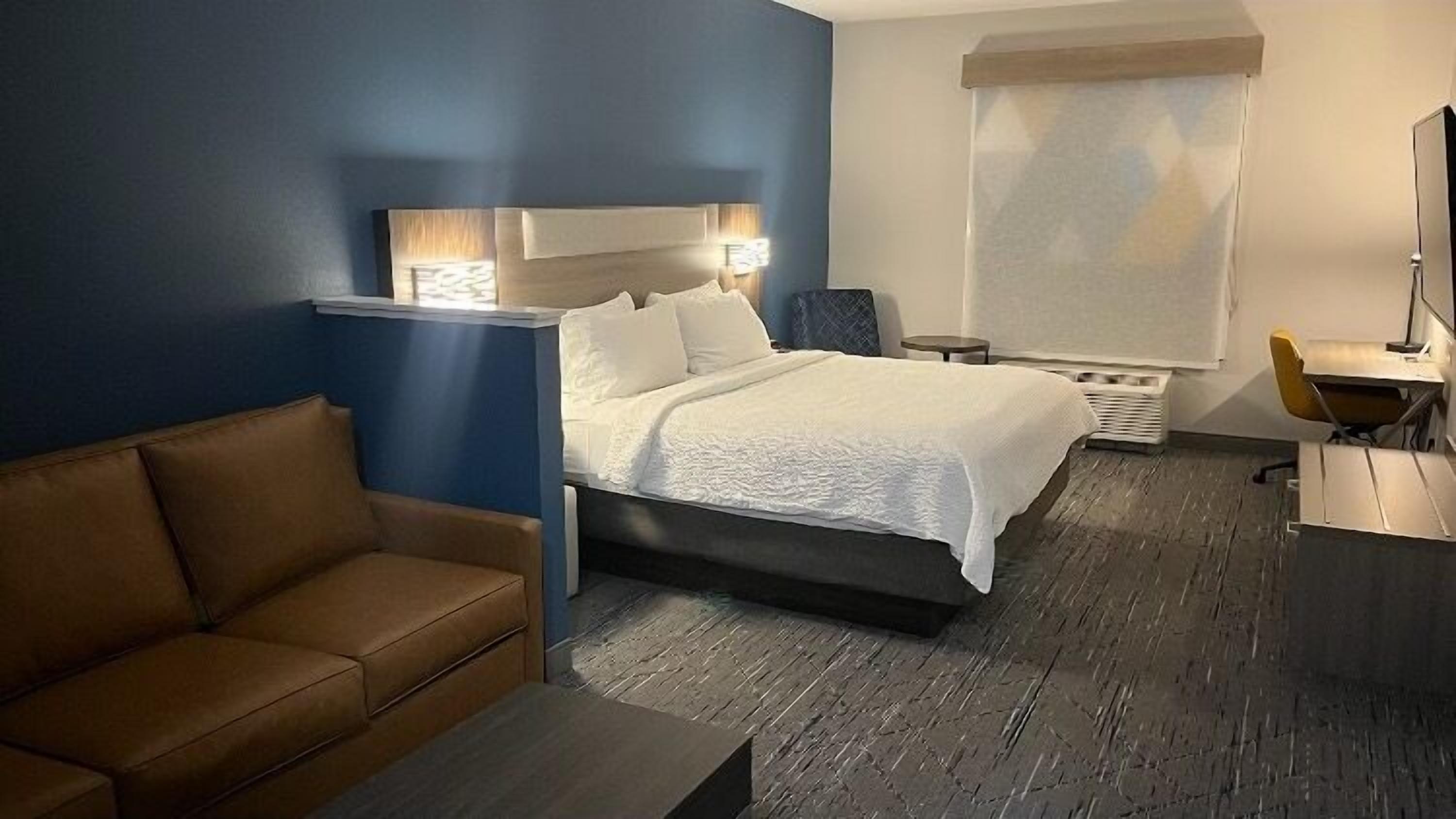 Una habitación de hotel con una cama, un sofá marrón, una mesita, un escritorio y una silla.