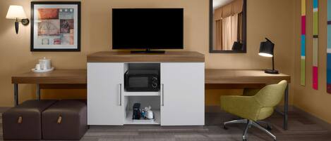 A hotel room with a flat-screen TV, a desk, a chair, a lamp, a coffee maker, and a microwave.
