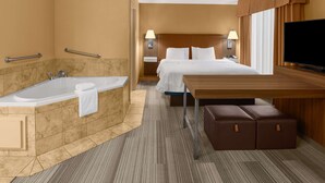 Ein Hotelzimmer mit einem großen Bett, einem Holztisch, einem Flachbildfernseher, einem Badezimmer mit Badewanne und Handläufen.