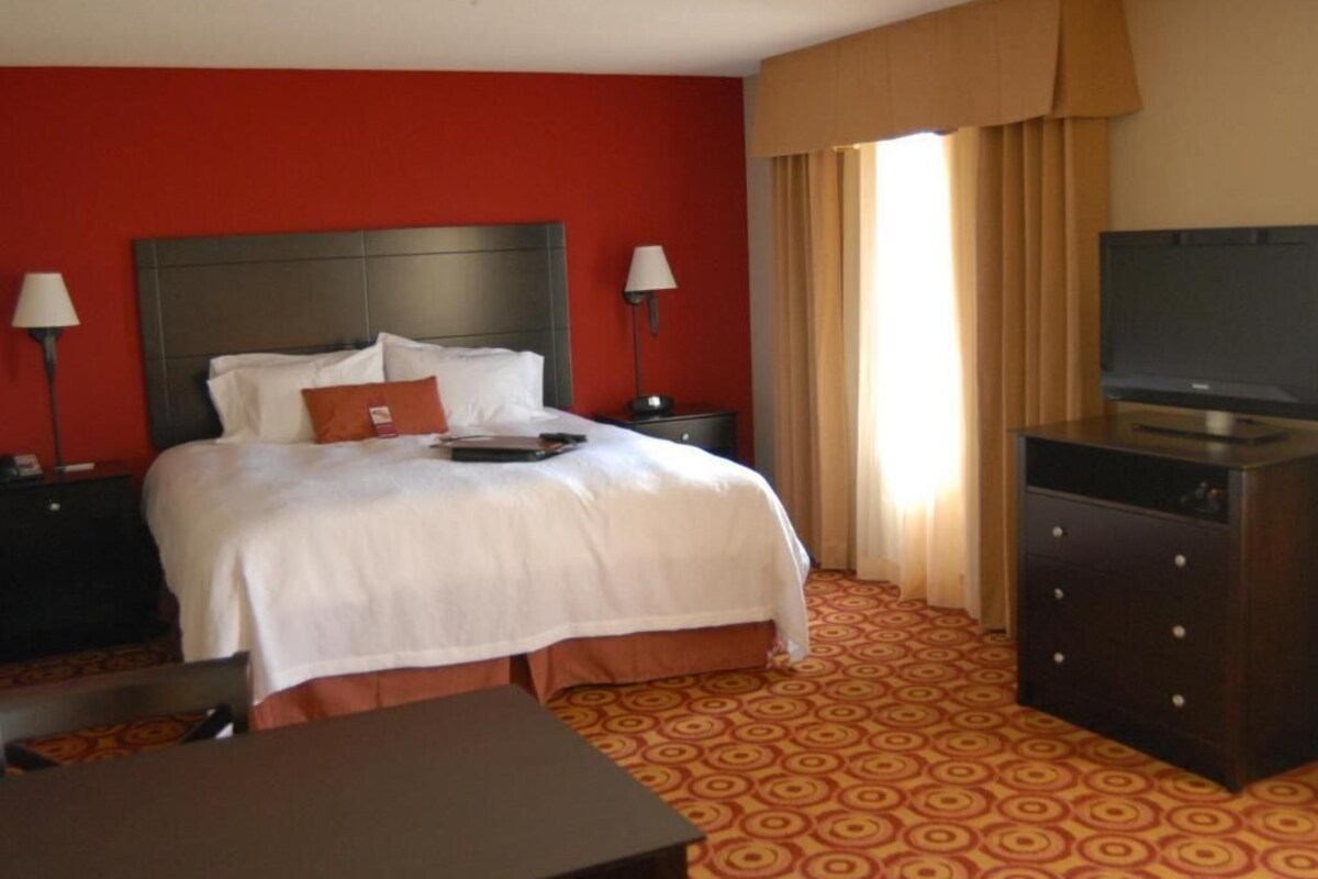 A hotel room with a bed, a desk, a dresser, a TV, and two lamps.