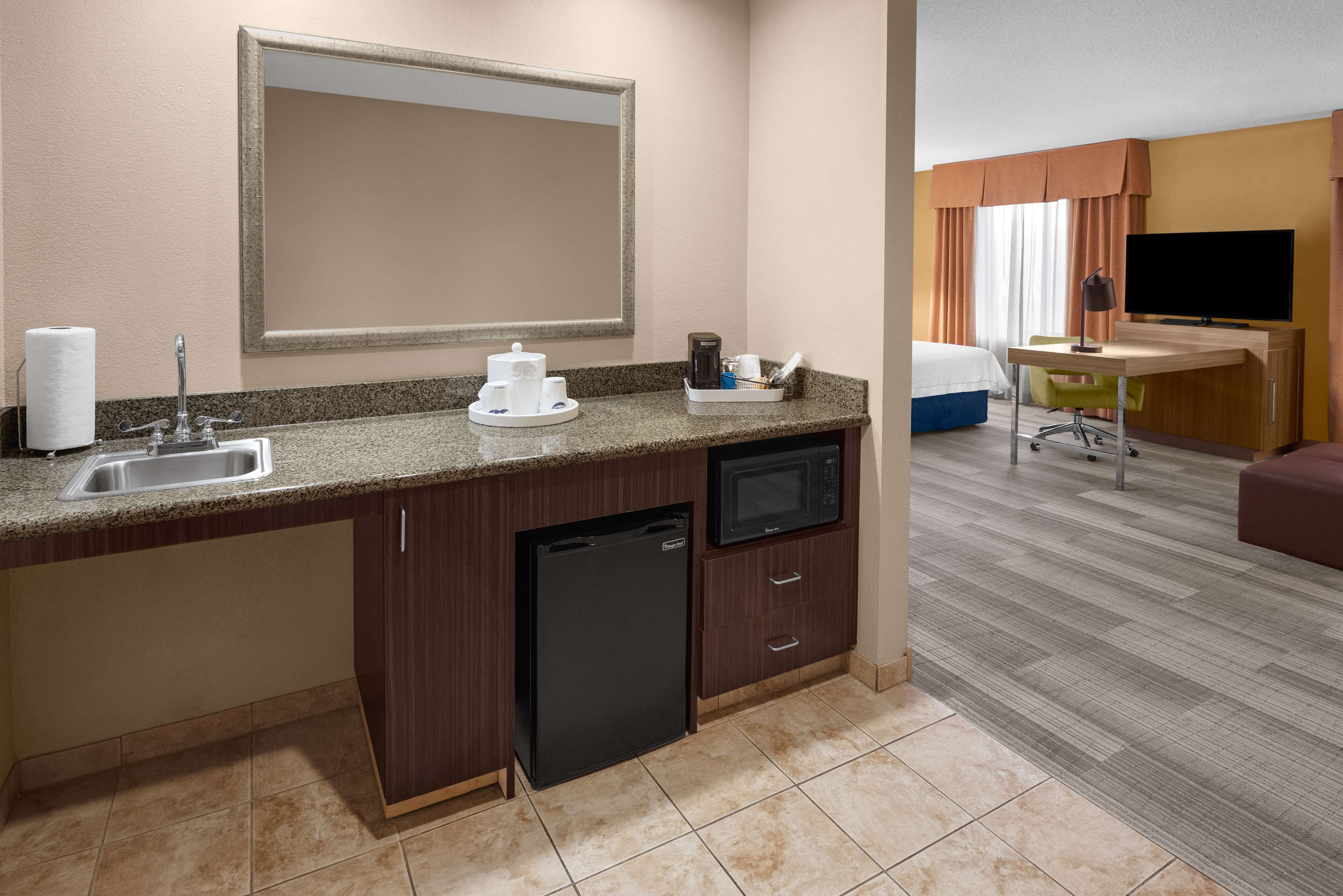 Une chambre d’hôtel équipée d’une kitchenette, d’un évier, d’un four à micro-ondes, d’un petit réfrigérateur, d’une télévision à écran plat, d’un bureau et d’une chaise.