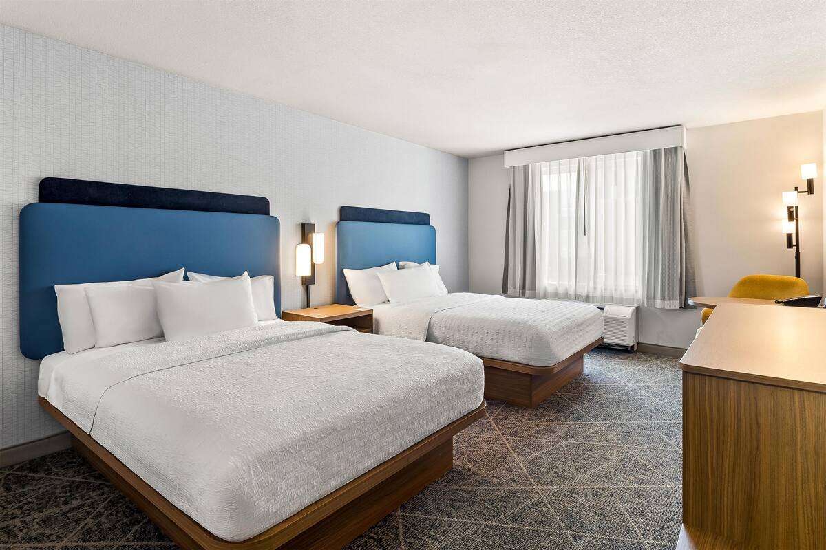 A hotel room with two beds, a desk, and a chair.