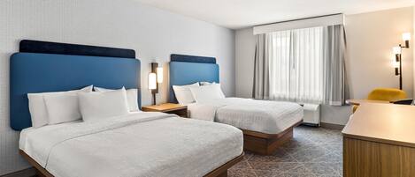 A hotel room with two beds, a desk, and a chair.