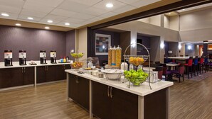 A hotel breakfast area with a buffet counter, various food stations, and seating arrangements.