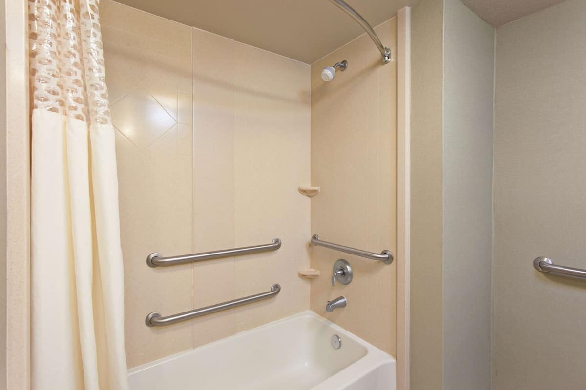 A bathroom with a bathtub, a shower, and grab bars for accessibility.