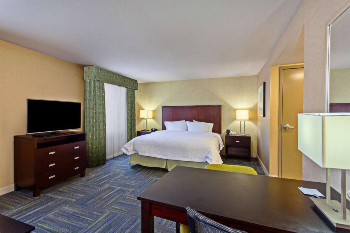 A hotel room with a bed, bedside tables, a TV, a desk, and a chair.