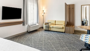 Una moderna camera d'albergo con televisore a schermo piatto montato a parete, un divano, un tavolino e un tappeto decorato.