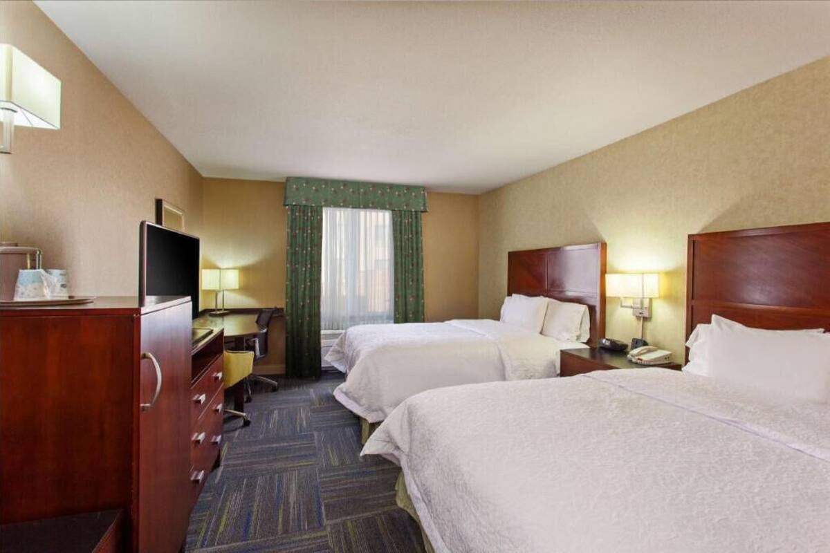 A hotel room with two beds, a desk with a chair, a television, and a lamp.
