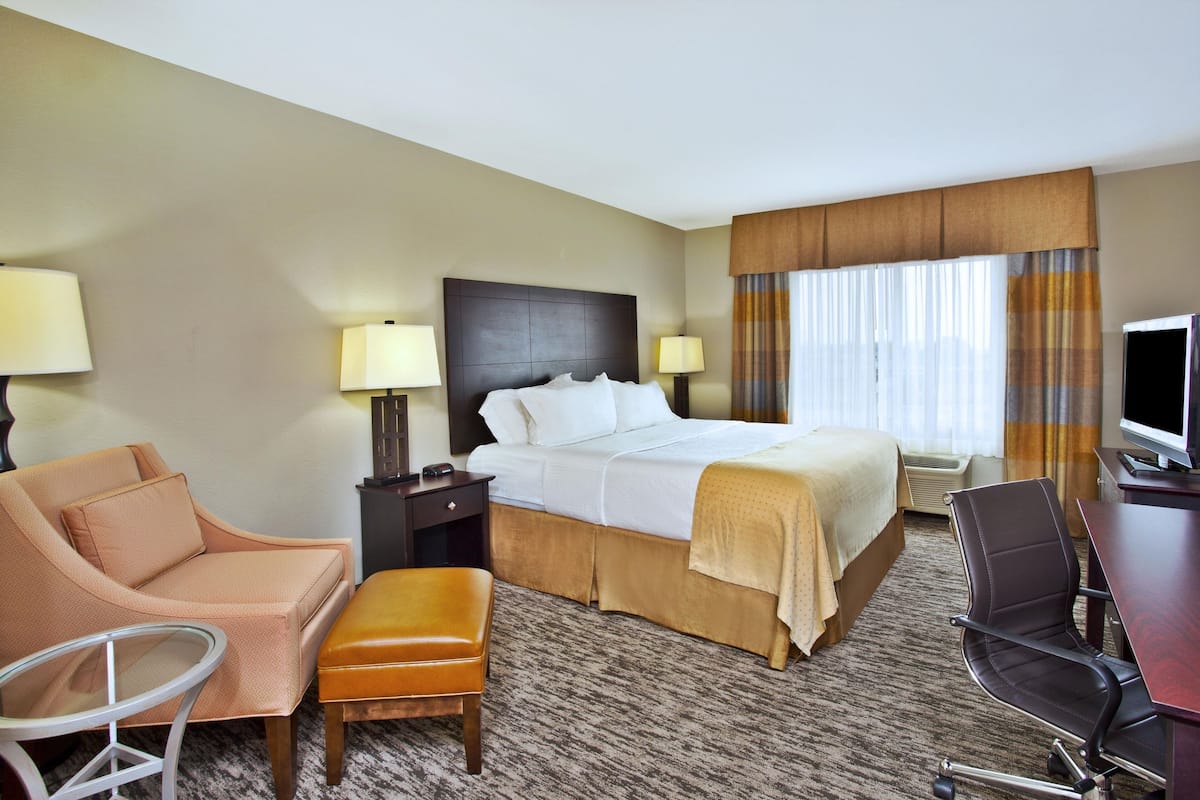 A hotel room with a bed, a sofa, an armchair, a desk, and a television.