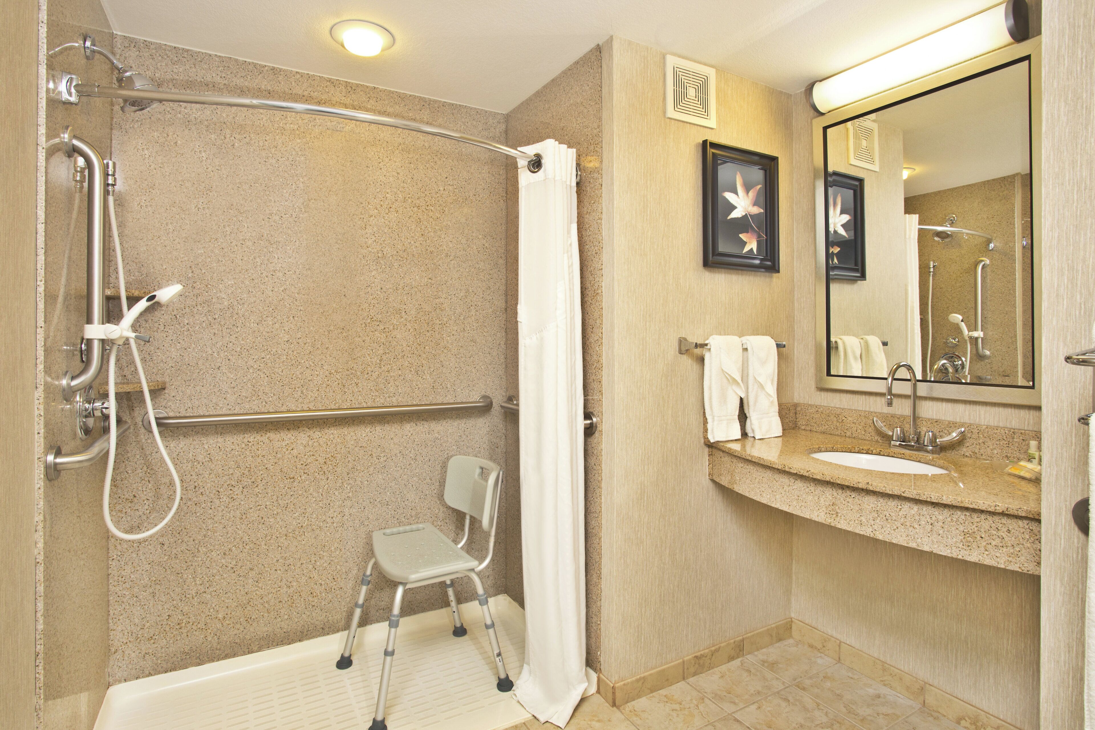 Ein Badezimmer mit Dusche, Toilette, Waschbecken, Spiegel und einem Sessel.