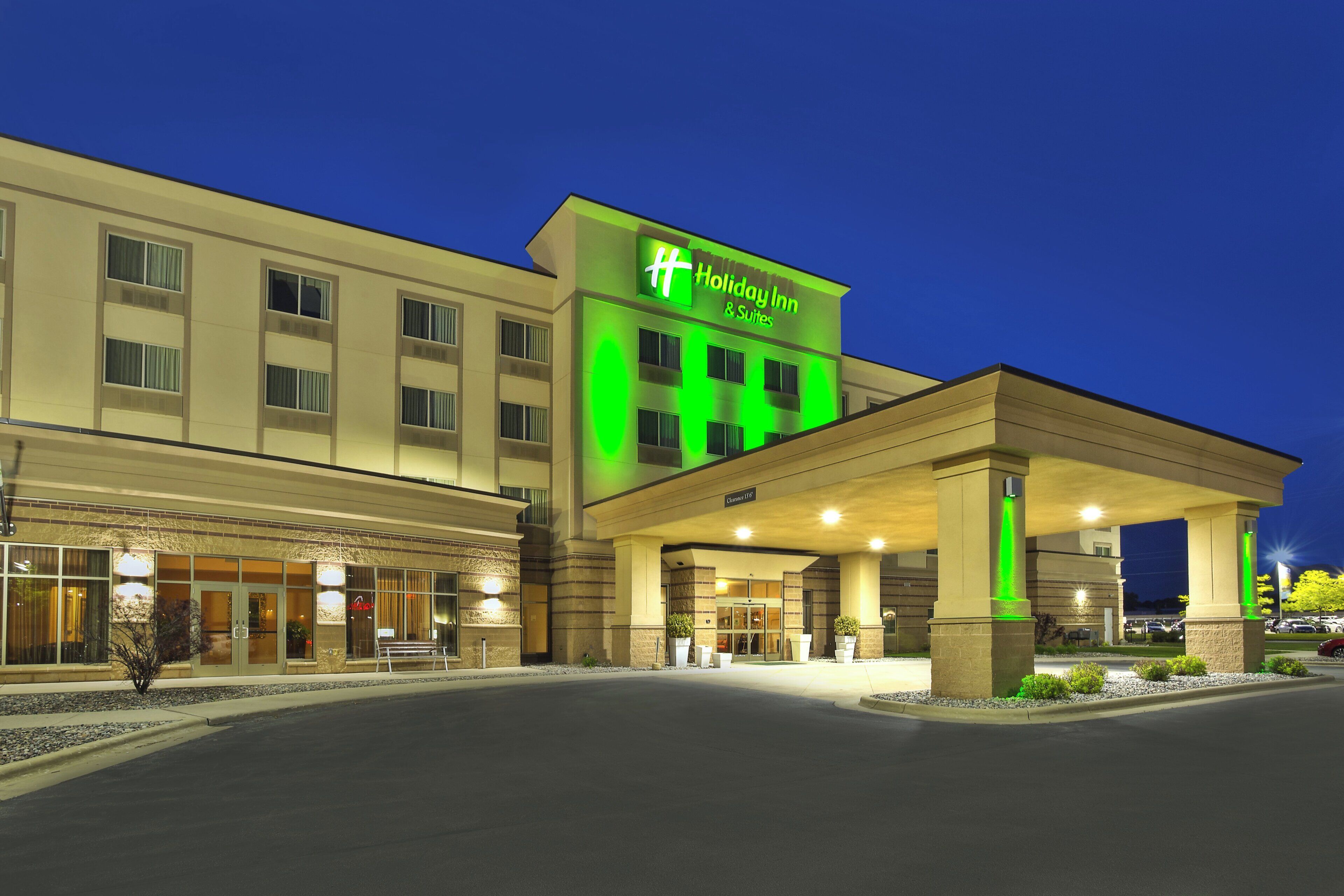 A Holiday Inn & Suites with a clear entrance, a parking lot, and a well-lit facade.