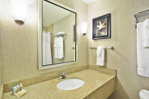 A hotel bathroom with a large mirror, a sink, and a towel rack. - Holiday Inn & Suites Green Bay Stadium by IHG (Green Bay)