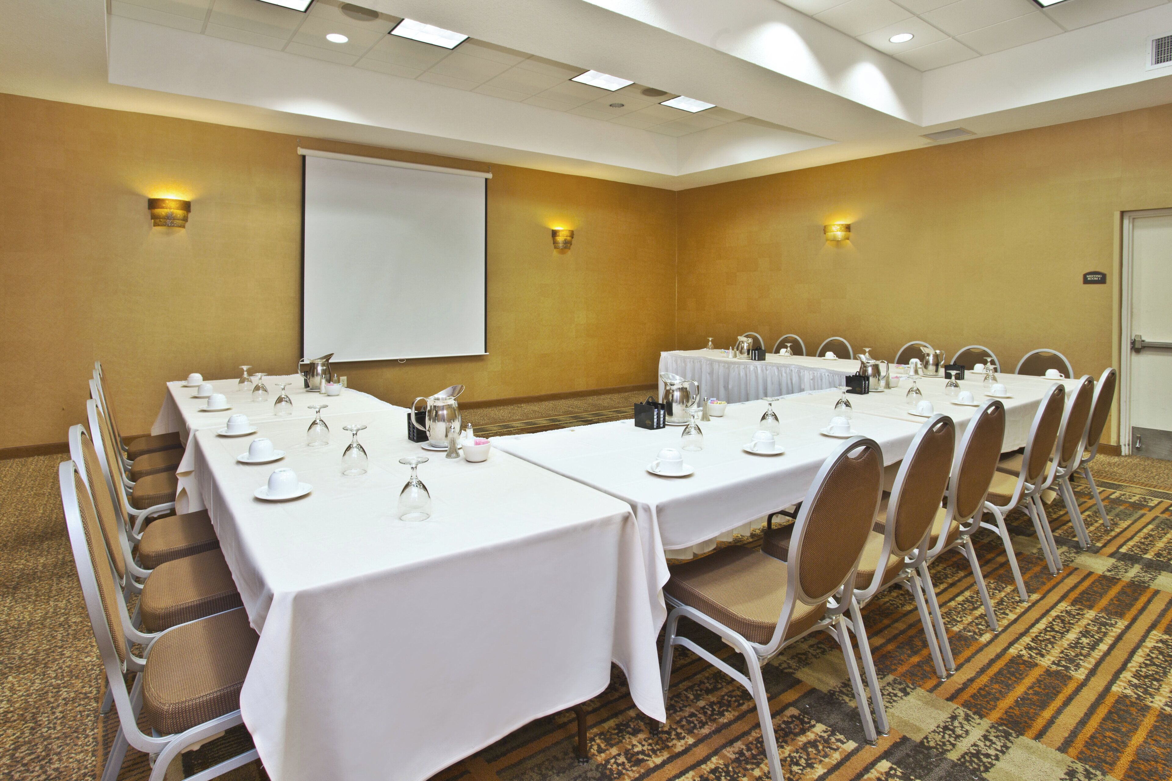 A conference room with a long table set for a meeting, equipped with chairs, tables, and a projector screen.