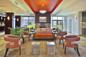 A hotel lobby with a sofa, armchairs, a bar, and a dining area.