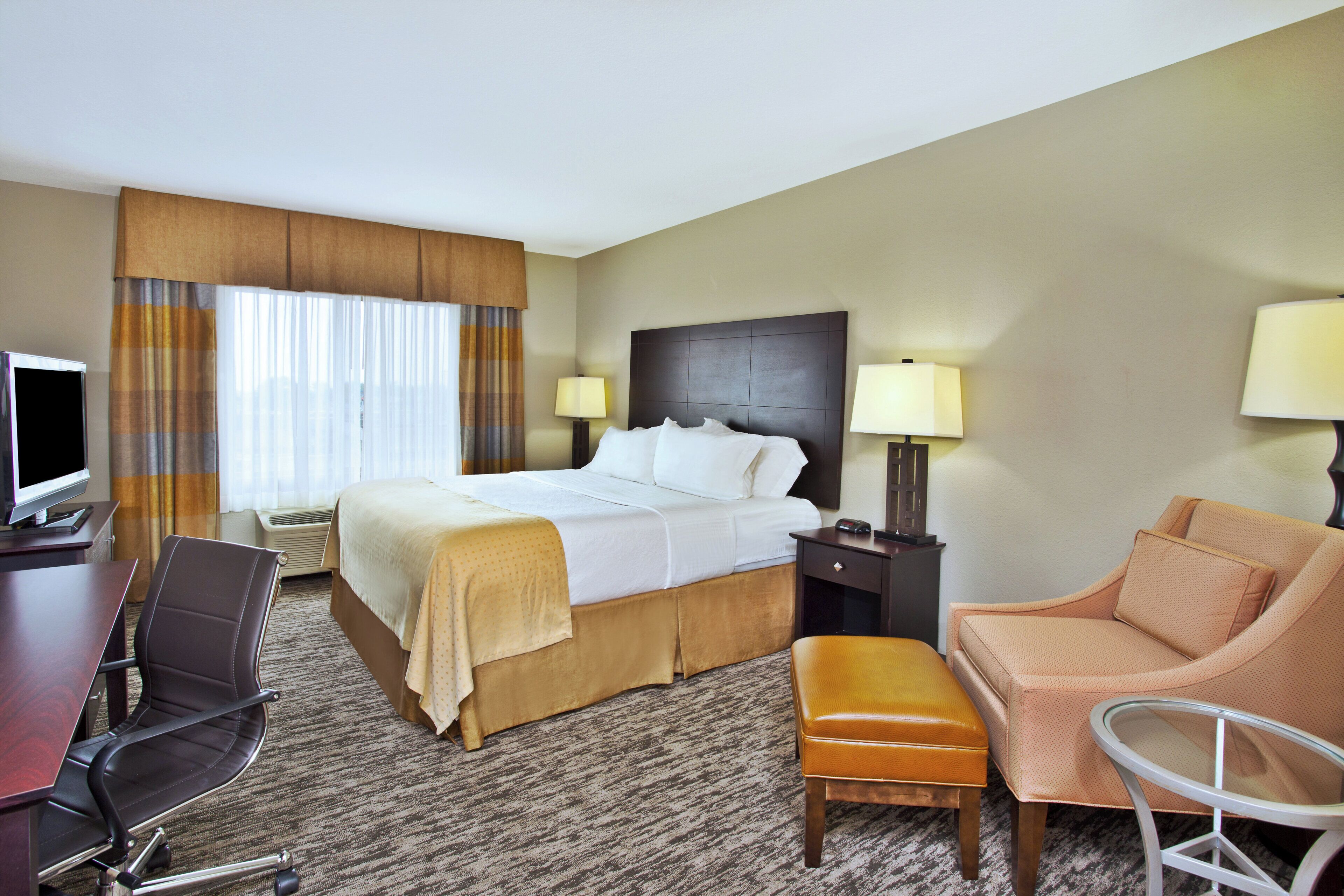 A hotel room with a bed, desk, chair, sofa, and lamps.
