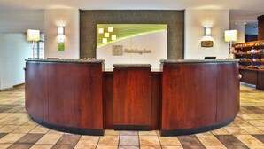 A reception desk with a 'Holiday Inn' sign, a plaque, and a snack bar in the background. - Holiday Inn & Suites Green Bay Stadium by IHG (Green Bay)