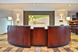 Una mesa de recepción con un letrero de 'Holiday Inn', una placa conmemorativa y una barra de aperitivos al fondo.