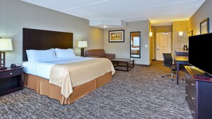 A hotel room with a large bed, a desk, a chair, a television, and a lamp.