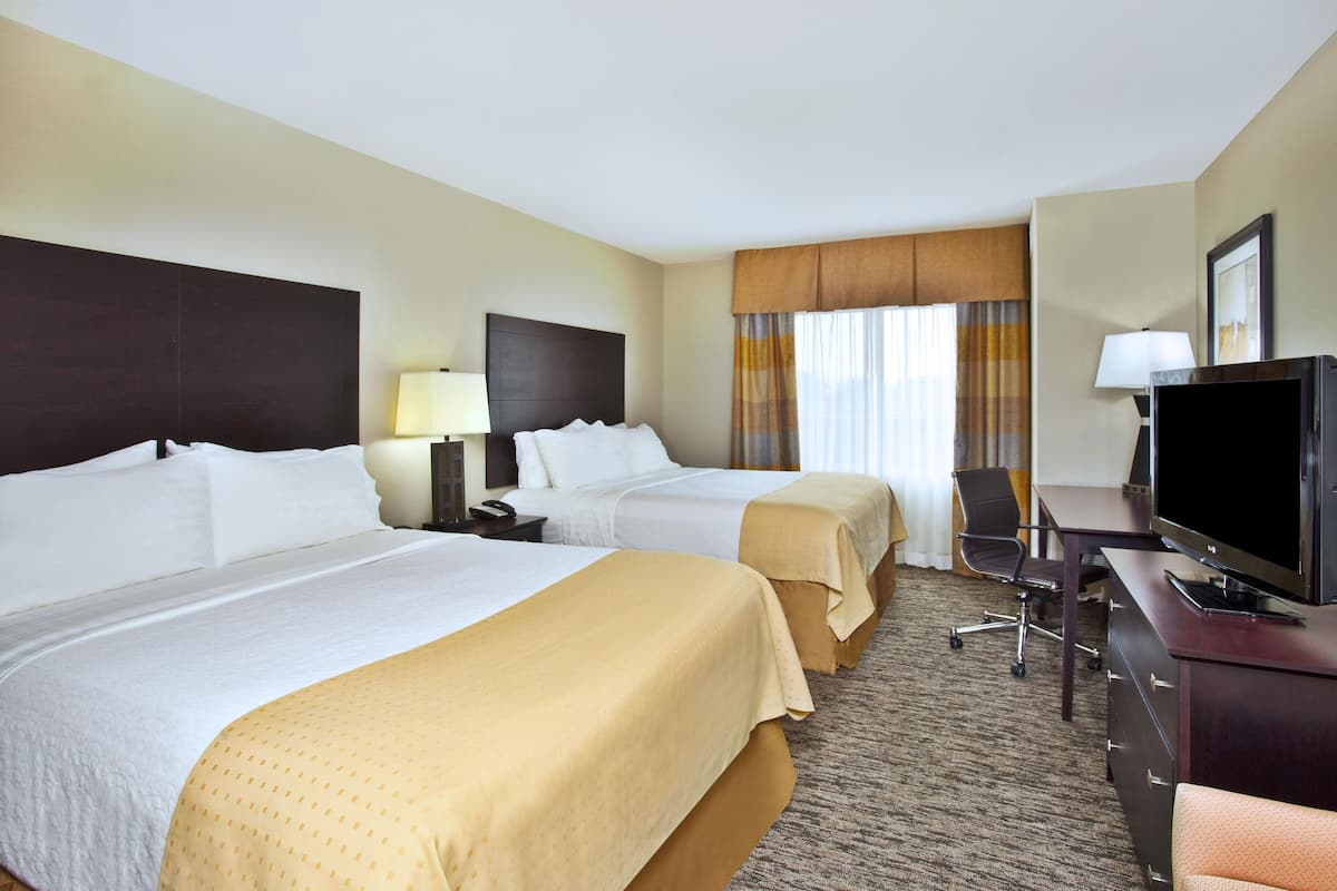 A hotel room with two beds, a desk with a television, and a chair.