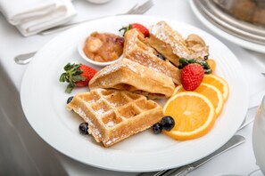 A plate of waffles with strawberries, blueberries, and orange slices. - Holiday Inn & Suites Green Bay Stadium by IHG (Green Bay)