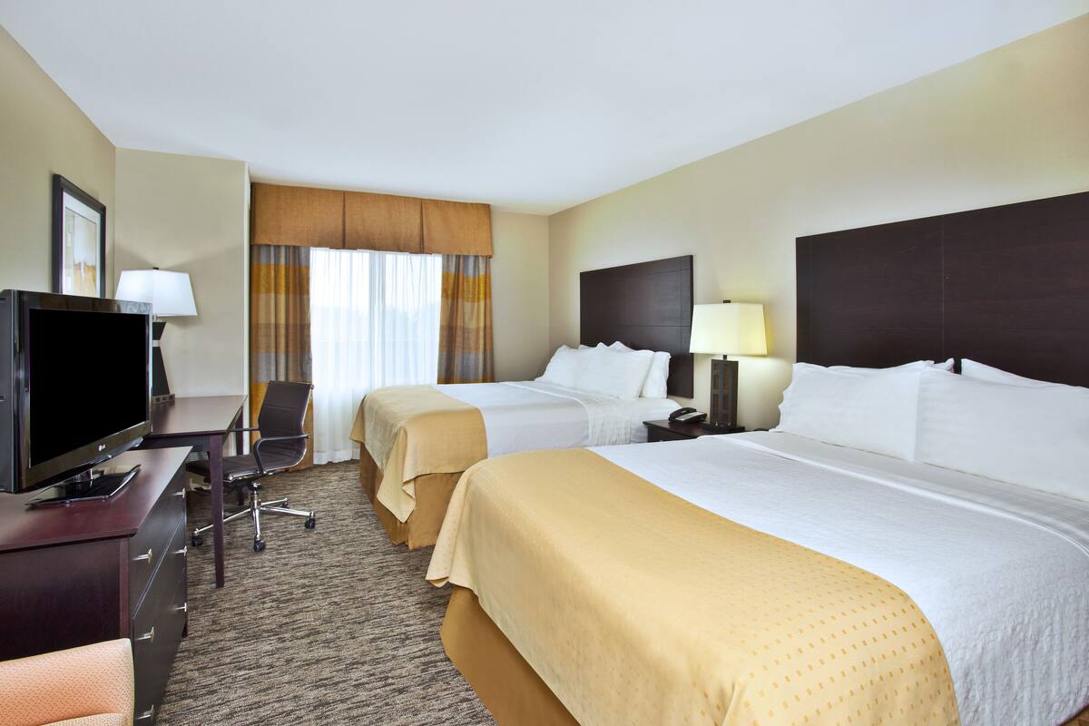 A hotel room with two beds, a desk with a TV, and a chair.