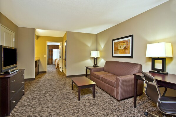 A hotel room with a sofa, a TV, a desk, and a lamp. - Holiday Inn & Suites Green Bay Stadium by IHG (Green Bay)