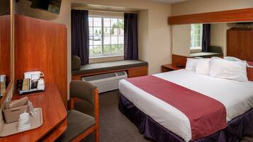 A hotel room with a large bed, a desk with a chair, a window with curtains, a television mounted on the wall, and a small table with a tray.