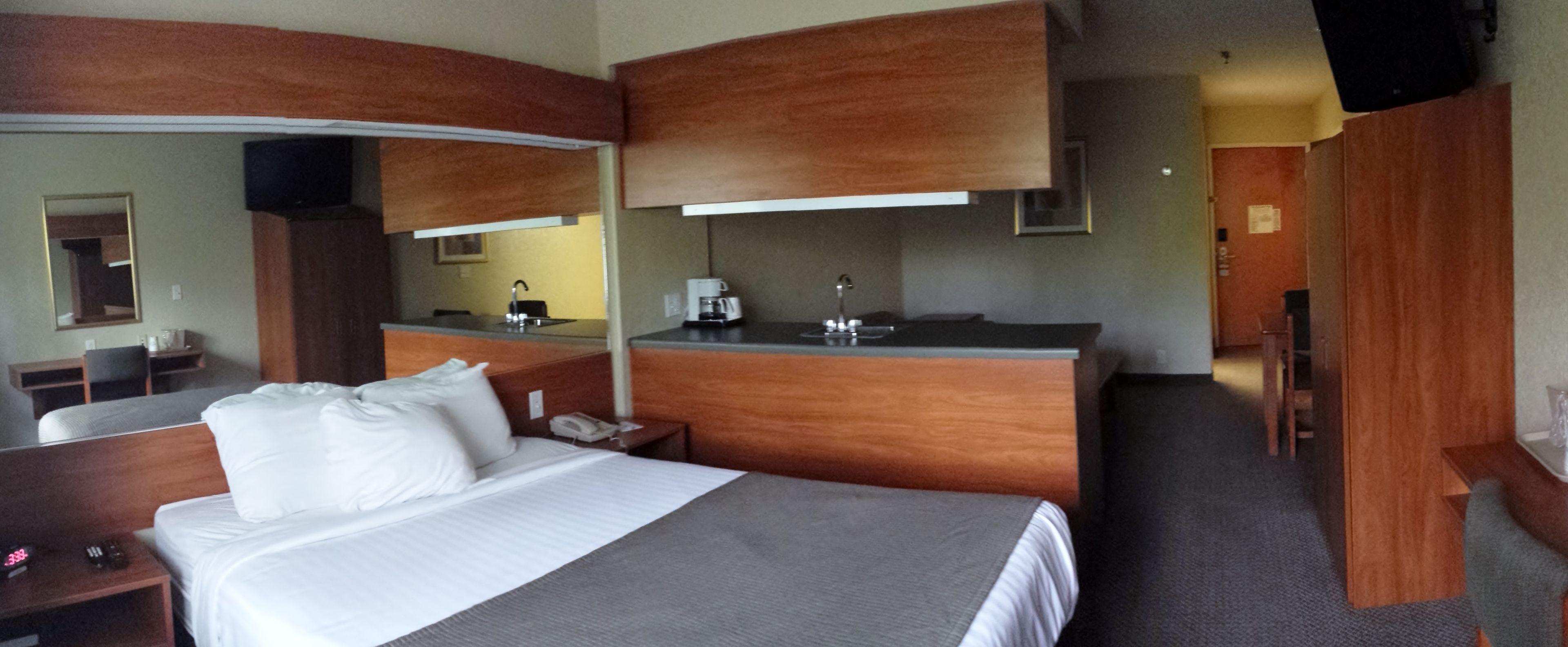 A hotel room with a bed, a desk, a mirror, a kitchenette, and a bathroom.