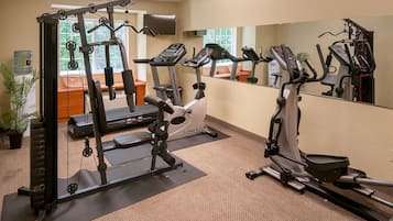 Een sportschool met cardioapparatuur, krachttoestellen en een spiegel.