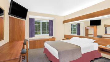 Habitación de hotel con cama, escritorio con silla, televisor montado en la pared y ventana con cortinas.