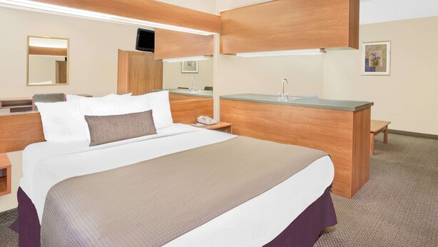 Camera d'albergo con un letto grande, una testiera in legno, un comodino con un telefono, una piccola scrivania con uno specchio e un quadro appeso al muro.