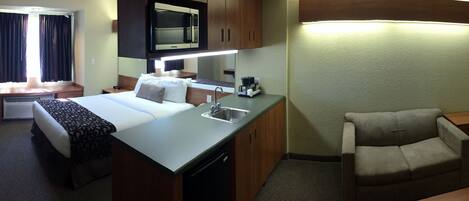 Habitación de hotel compacta con kitchenette, una cama con almohada, un sofá y una pequeña mesa.