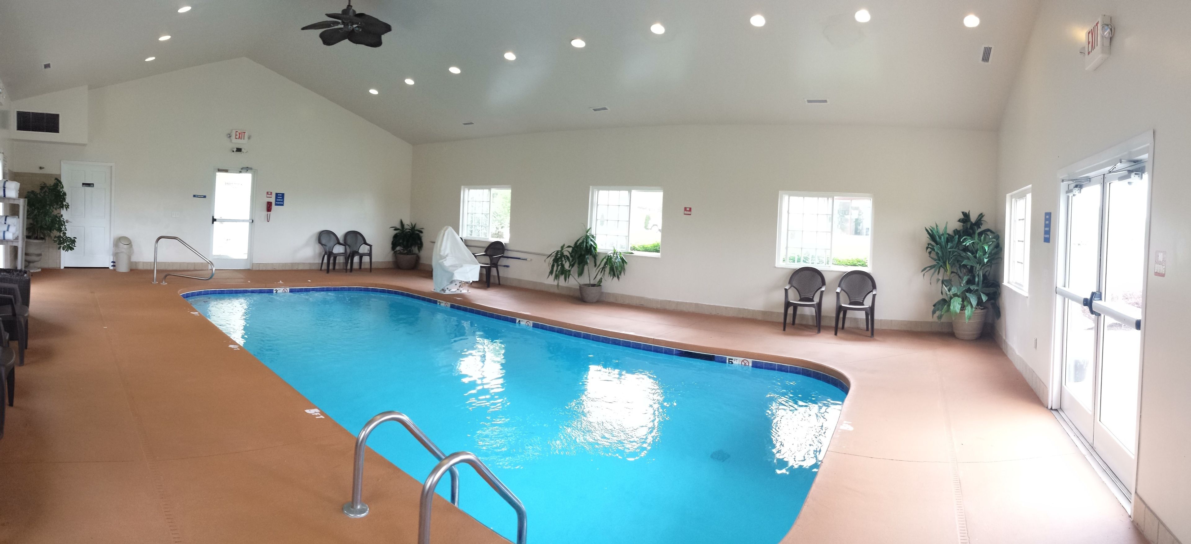 An indoor swimming pool with clear water, surrounded by chairs and potted plants.