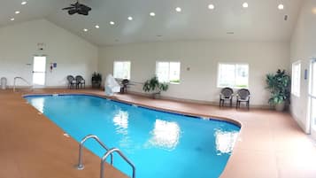 An indoor swimming pool with clear water, surrounded by chairs and potted plants.