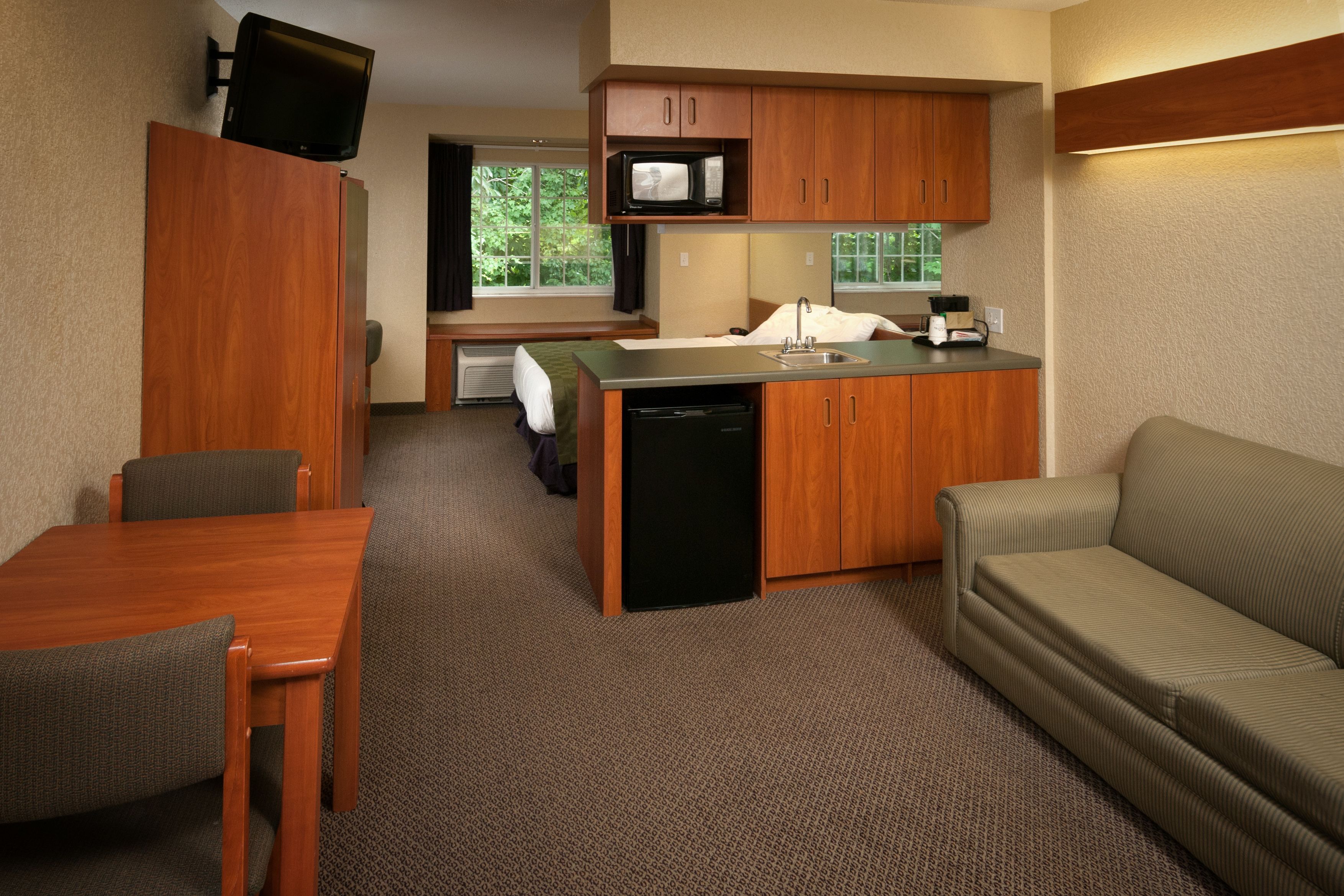 A compact hotel room with a kitchenette, a dining area, and a sofa.