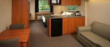 A compact hotel room with a kitchenette, a dining area, and a sofa.