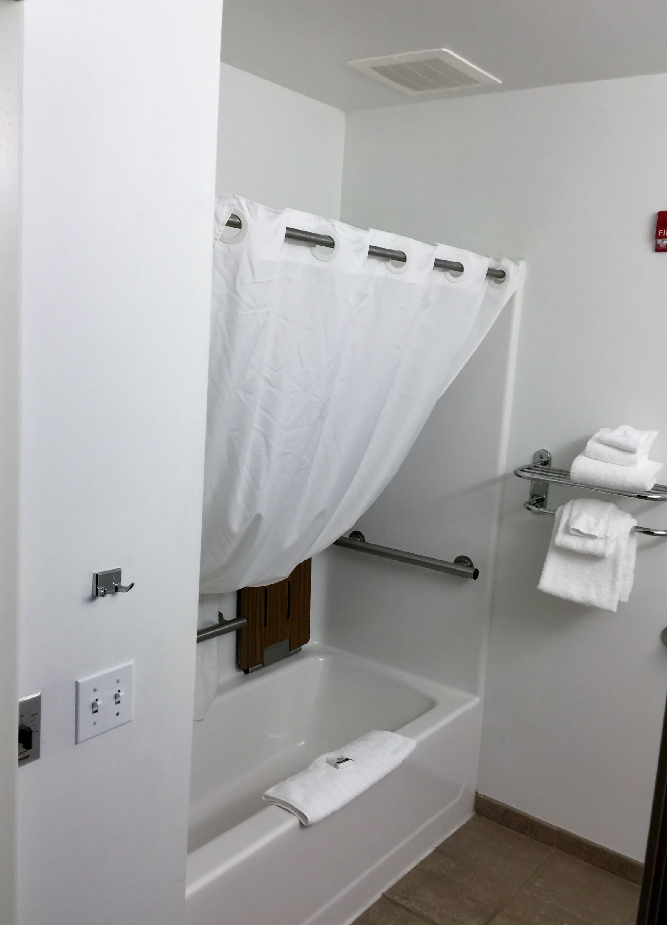 A bathroom with a bathtub, a shower curtain, a towel rack, and a towel dispenser.