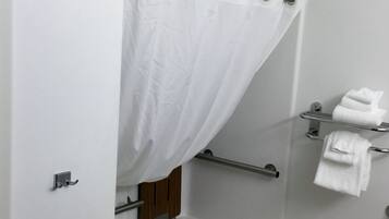 A bathroom with a bathtub, a shower curtain, a towel rack, and a towel dispenser.